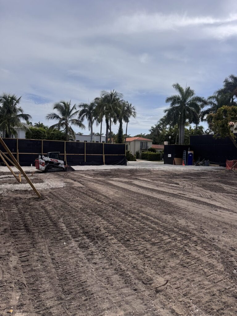 Skid steer grading a South Florida lot after a full structural teardown, with the debris hauled off and the perimeter fenced.